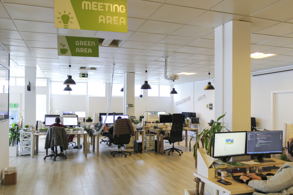 Ufficio a Tenerife con persone che lavorano ai computer. Cartelli: MEETING AREA, GREEN AREA.