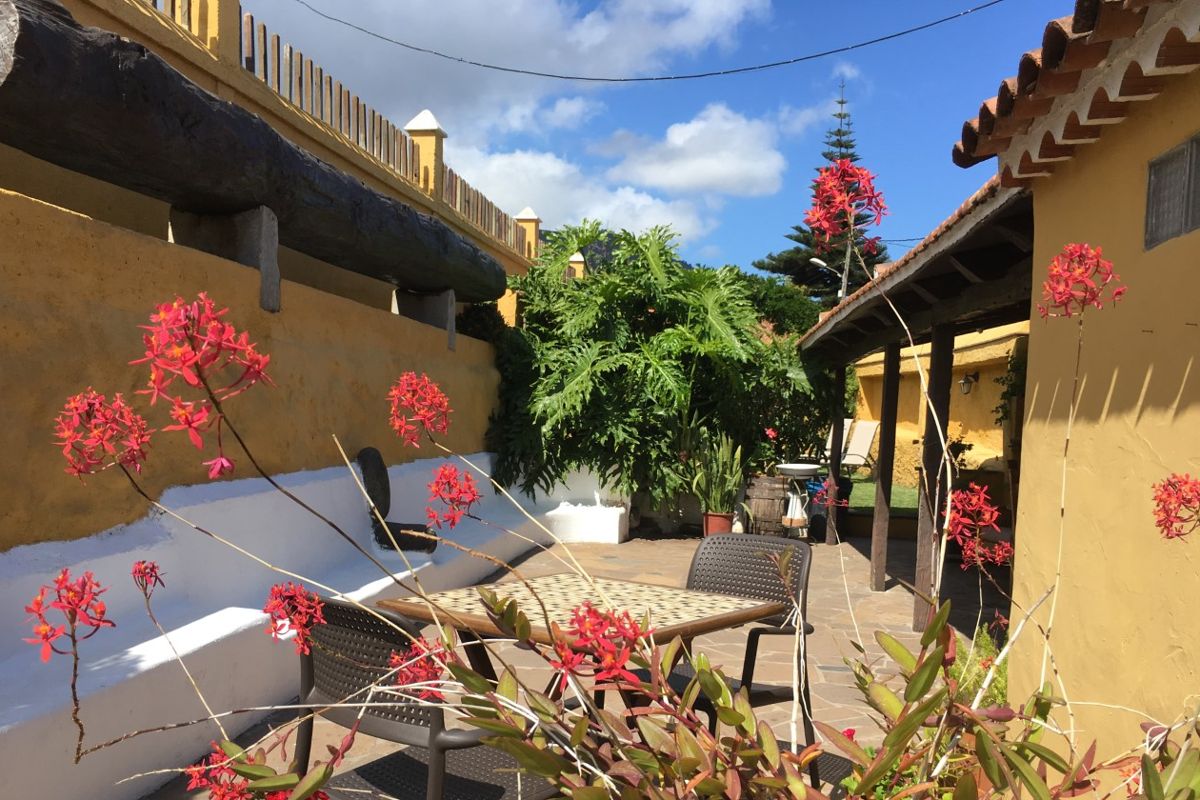 Cortile con sedie, tavolo e fiori rossi sotto cielo blu a Tenerife.