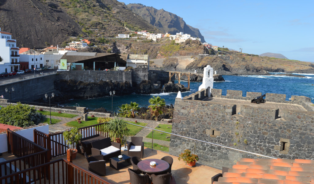 Vista del porto e delle montagne a Garachico, Tenerife, con mobili da terrazza in primo piano.