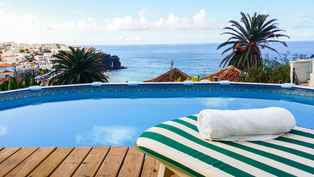 Piscina con vista sull'oceano e case a Garachico, Tenerife, con una palma.