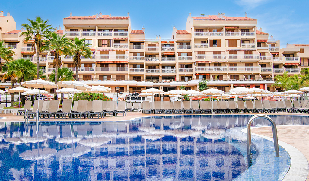 Piscina e sedie a sdraio con ombrelloni davanti a un hotel a Tenerife.