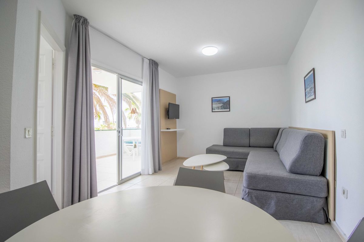 Soggiorno con divano grigio, tavoli e TV nel residence di Tenerife.