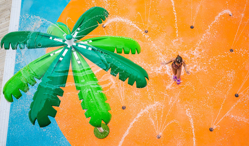 Bambina gioca nell'acqua sotto una palma artificiale a Tenerife.