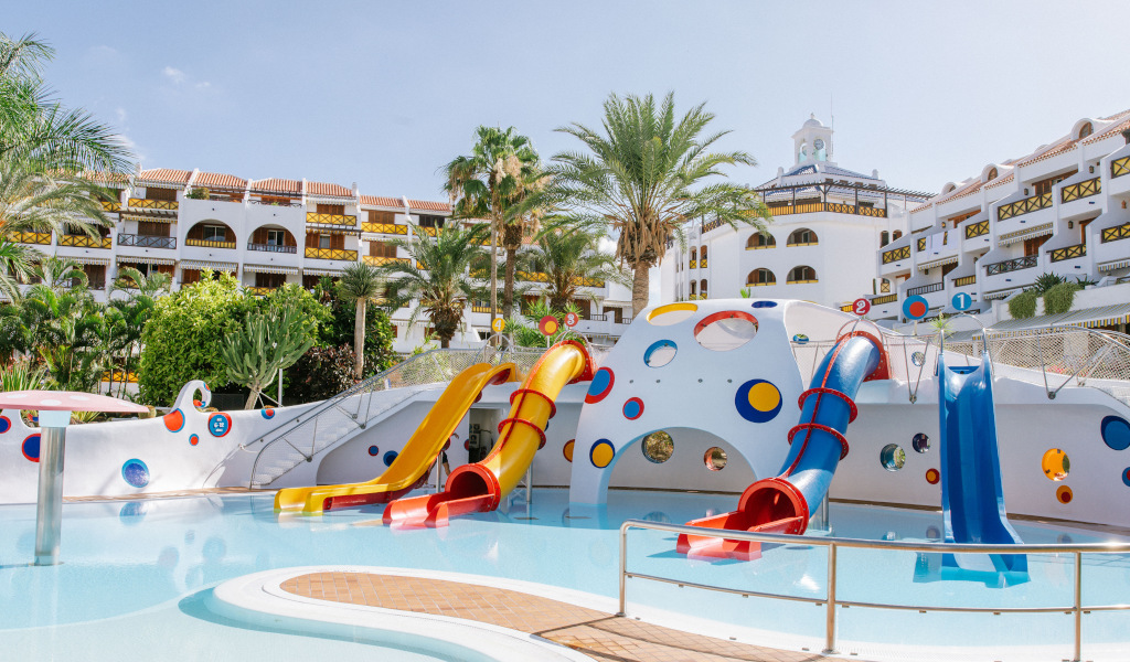 Piscina per bambini con scivoli colorati a Tenerife, circondata da palme.