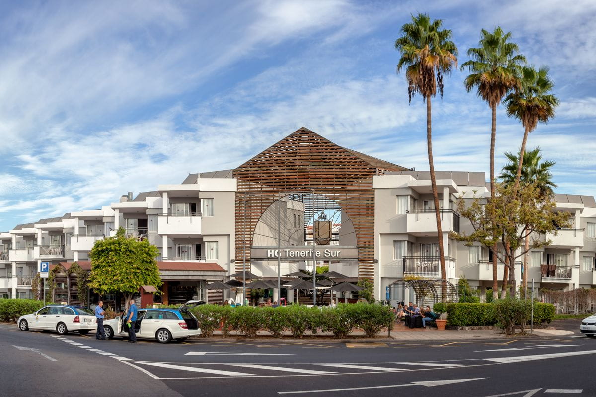 Edificio HC Tenerife Sur con palme e auto parcheggiate di fronte.