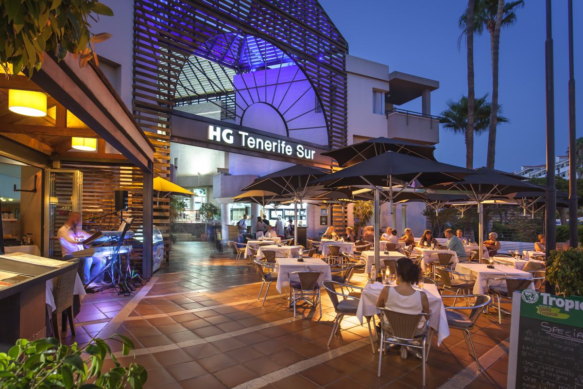 HG Tenerife Sur di notte con ristorante all'aperto e persone sedute sotto ombrelloni.