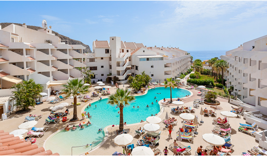 Piscina del resort con turisti e sdraio a Tenerife, vista sull'oceano.