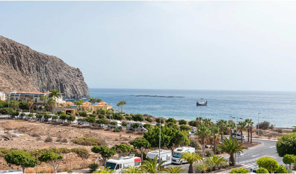 Spiaggia di Los Cristianos, Tenerife, con barca sul mare e scogliere rocciose.