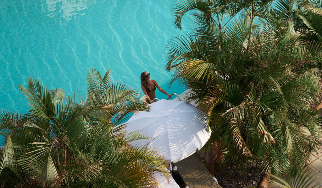 Donna in piscina a Tenerife, accanto a ombrellone bianco e palme.