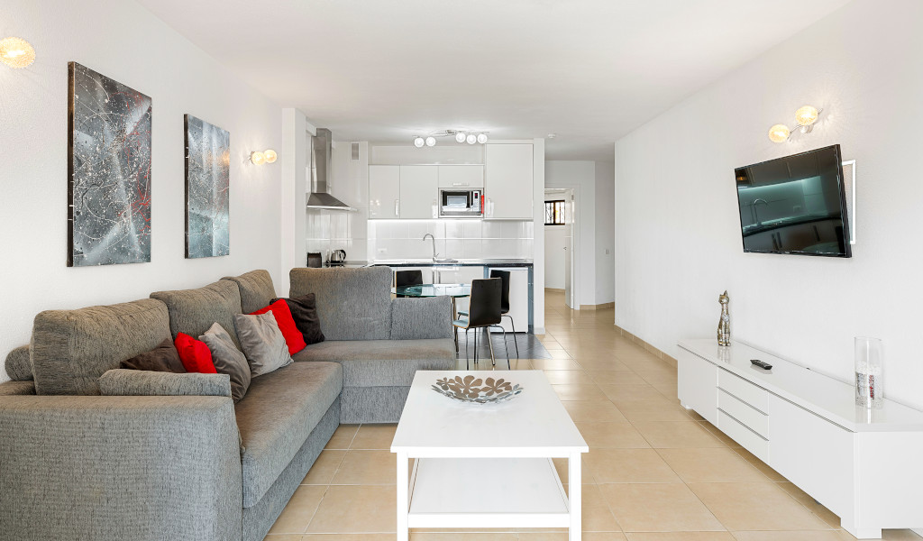 Soggiorno moderno con divano grigio, cucina a vista e TV a Costa Adeje, Tenerife.
