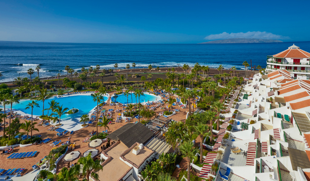 Piscina e spiaggia a Playa de las Américas, Tenerife, con palme e mare.