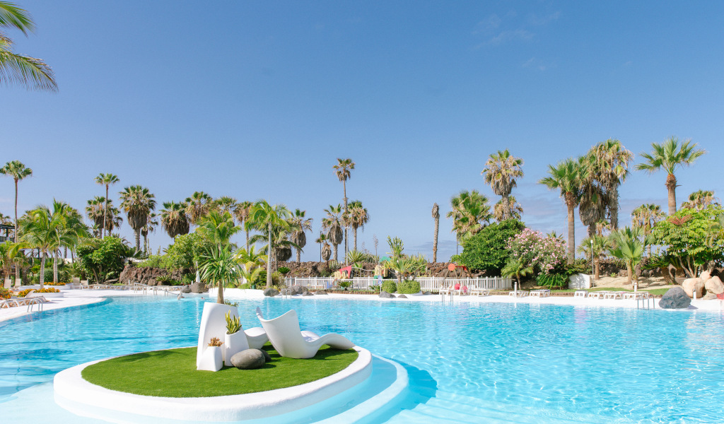 Piscina con palme e sedie bianche in un resort a Tenerife.