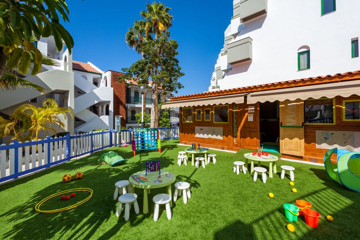 Area giochi per bambini all'aperto a Tenerife con tavolini, sedie e giochi su prato.