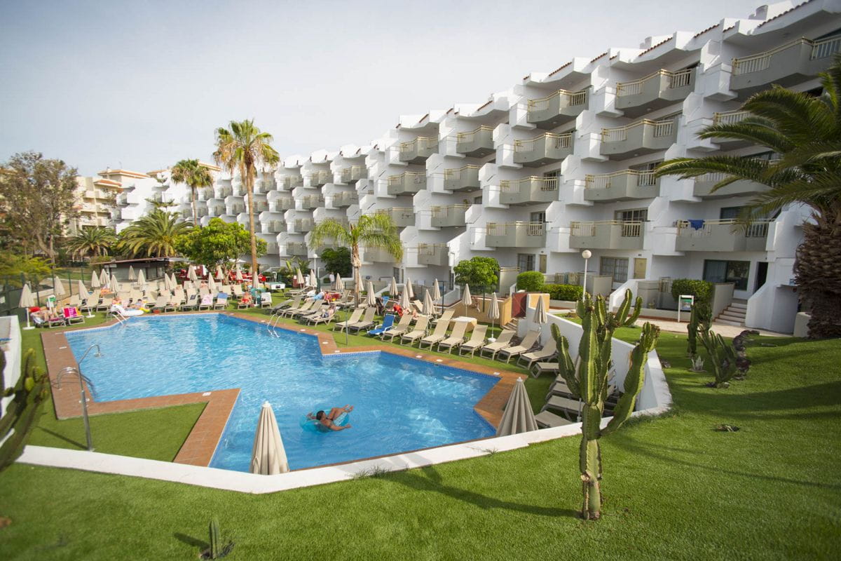 Piscina con sdraio e ombrelloni circondata da edifici e palme a Tenerife.