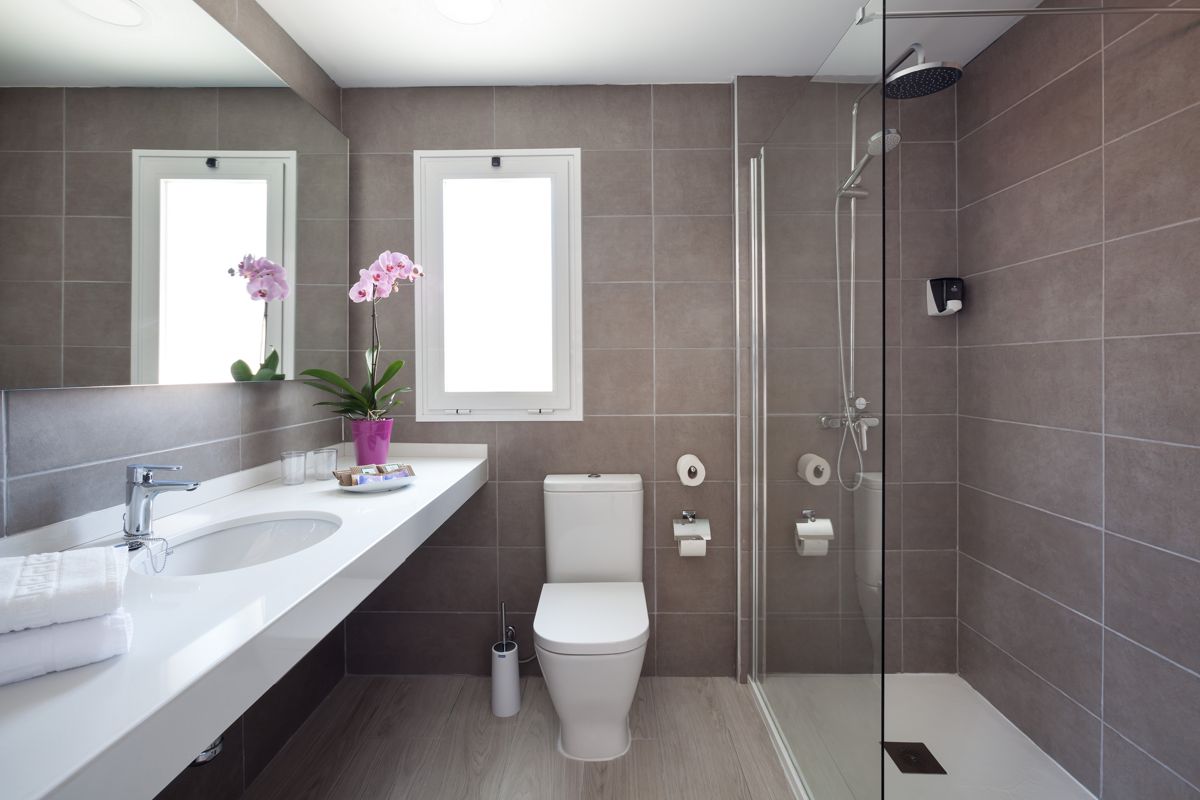 Bagno moderno con doccia, lavabo, toilette e orchidea in un vaso viola a Tenerife.