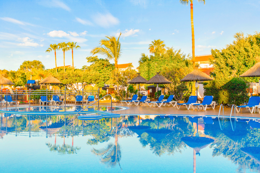Piscina con lettini e ombrelloni circondata da palme a Tenerife.