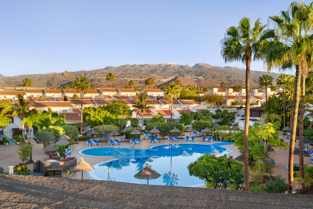 Piscina circondata da alberi e edifici bianchi con montagne sullo sfondo a Tenerife.