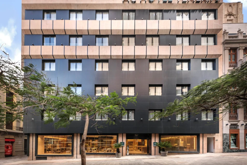 Edificio moderno ad Alicante con finestre a pannelli riquadri e alberi in primo piano.