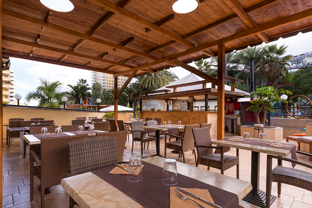 Terrazza di un ristorante a Tenerife con tavoli apparecchiati sotto un tetto in legno.