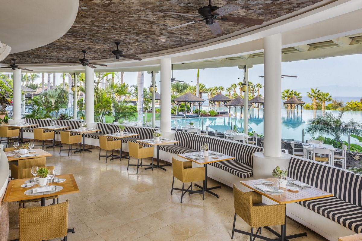 Terrazza ristorante con vista piscina a Tenerife, sedie e tavoli apparecchiati.