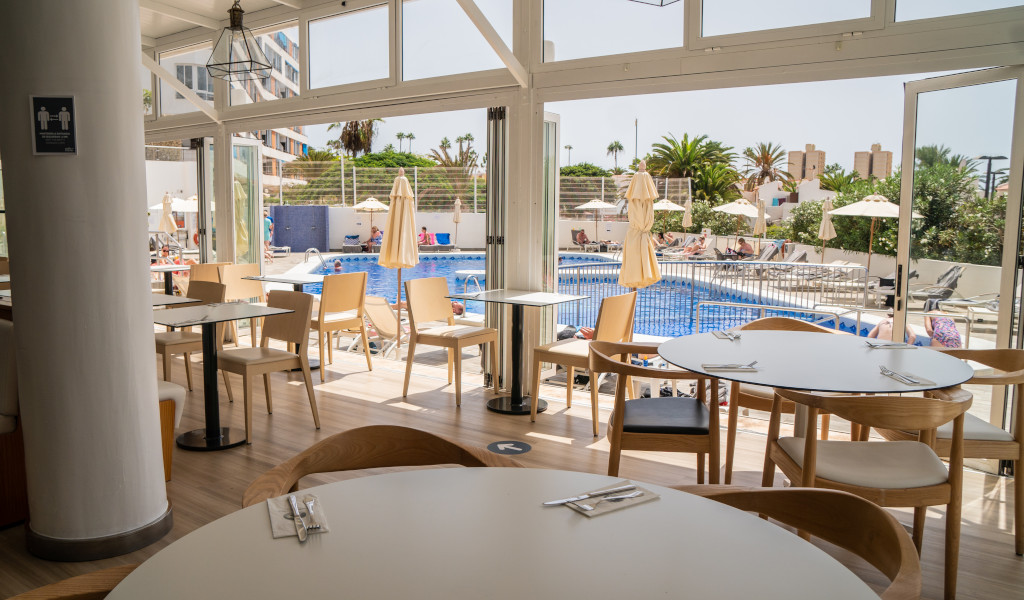 Ristorante con vista sulla piscina a Tenerife, tavoli apparecchiati e sedie.