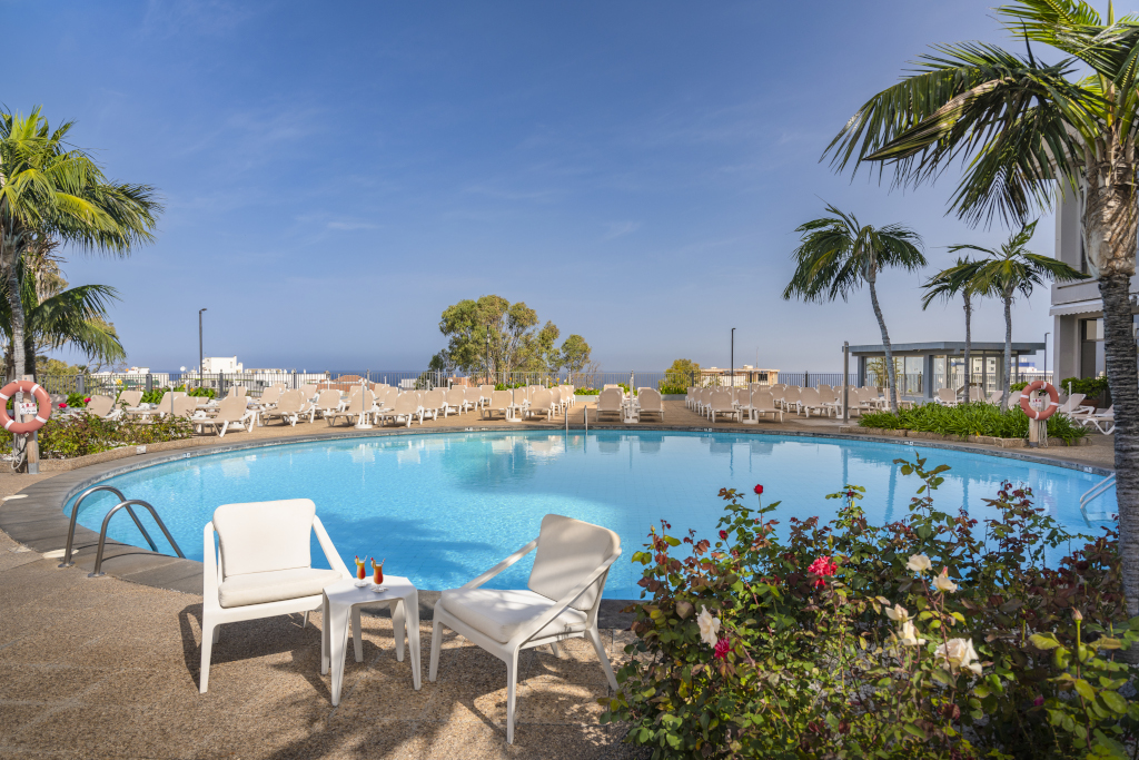 Piscina con sedie a sdraio e palme a Tenerife, vista mare sullo sfondo.