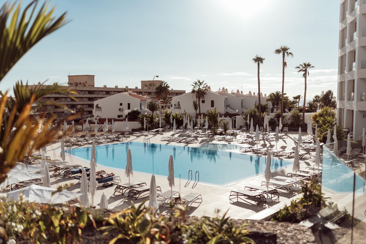 Piscina all'aperto con lettini e ombrelloni a Tenerife, circondata da palme.