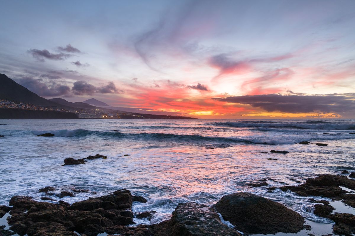 Tramonto sull'oceano a Puerto de la Cruz, Tenerife, con cielo colorato e rocce.