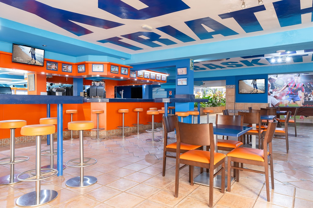 Bar sportivo colorato con sedie arancioni e foto di atleti nella parete a Tenerife.