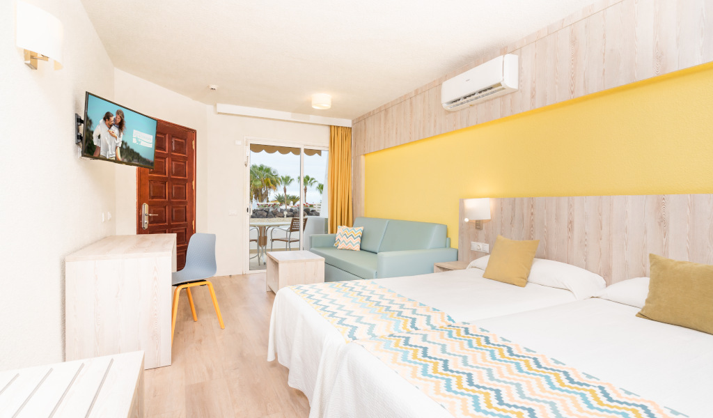 Camera d'albergo a Tenerife con due letti singoli, divano e balcone.