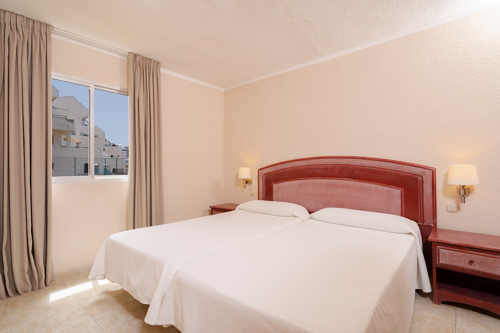 Camera da letto con due letti singoli a Tenerife, vista su edifici dal balcone.