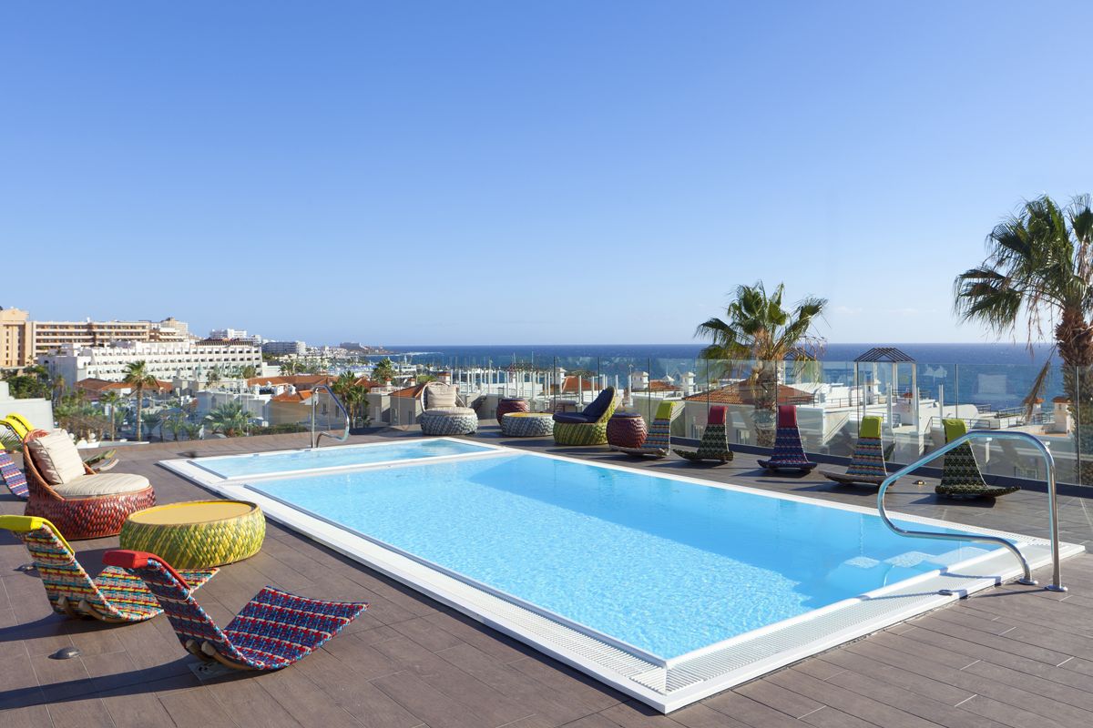 Piscina sul tetto con vista sull'oceano a Tenerife, circondata da sedie colorate.
