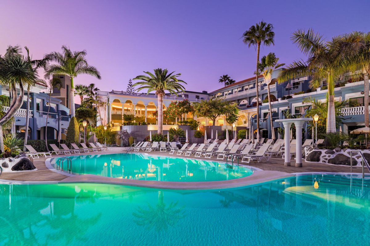 Piscina circondata da palme e sedie a sdraio in un resort a Tenerife.