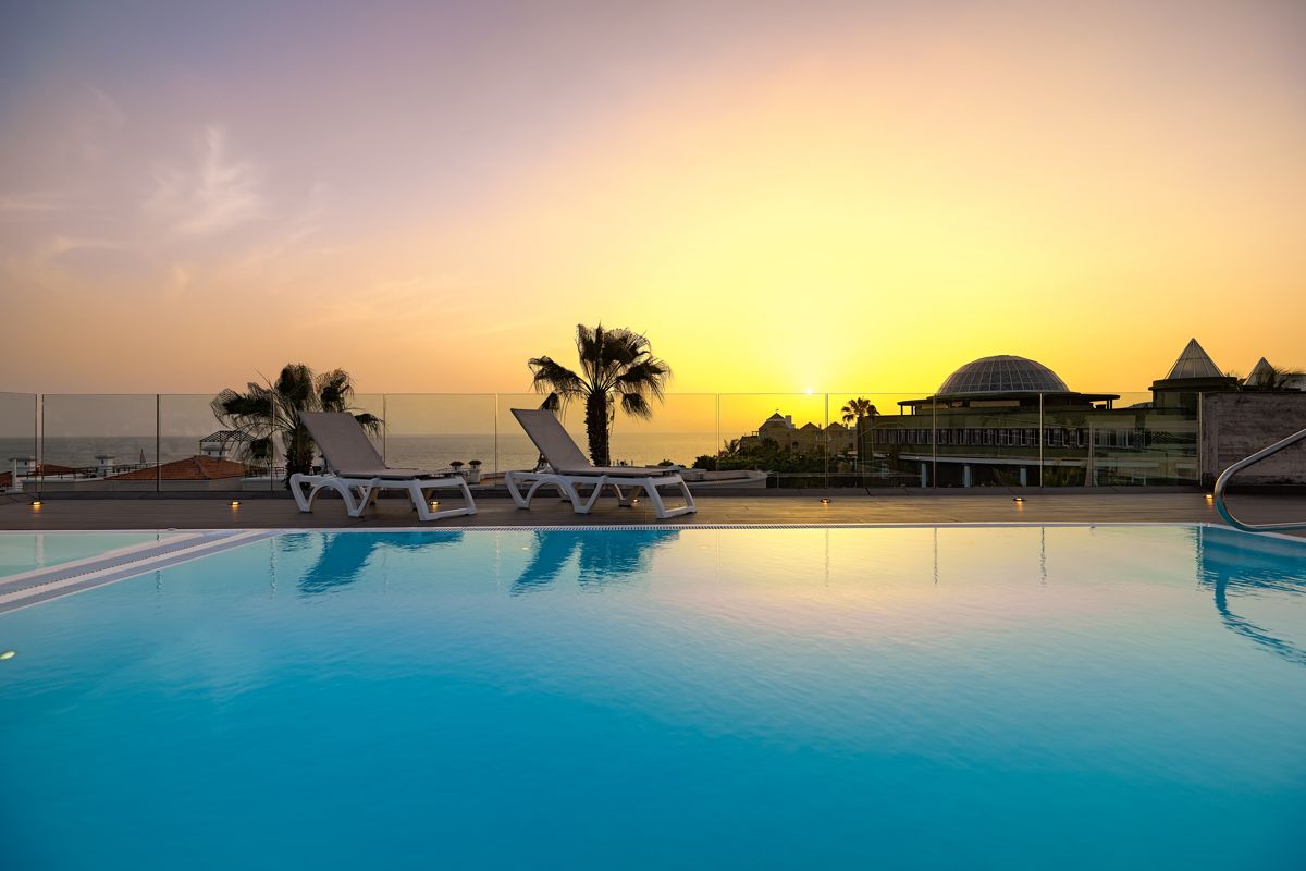 Piscina al tramonto con sdraio e palme a Tenerife.
