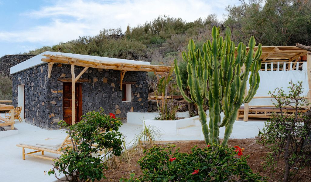 Casa in pietra lavica a Tenerife con cactus e sedie a sdraio nel giardino.