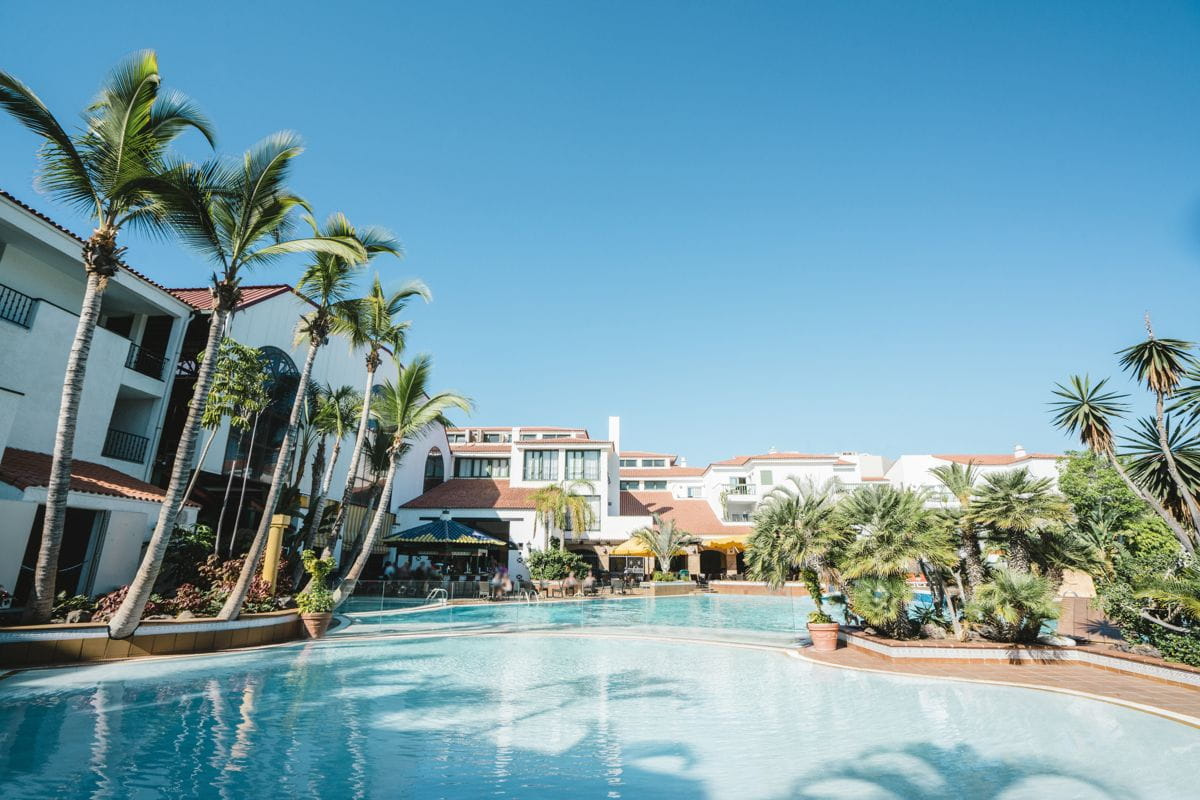 Piscina resort con palme a Tenerife sotto un cielo blu luminoso.