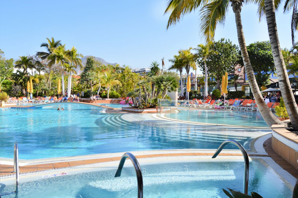 Piscina circondata da palme e lettini colorati a Playa de las Américas, Tenerife.