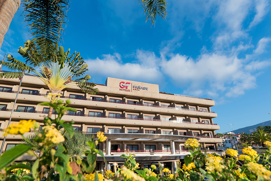 Edificio dell'hotel a Fanabe, Tenerife, circondato da palme e fiori gialli.