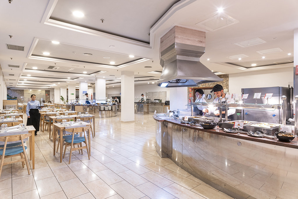 Ristorante a buffet in hotel a Tenerife con tavoli apparecchiati e cuochi al lavoro.