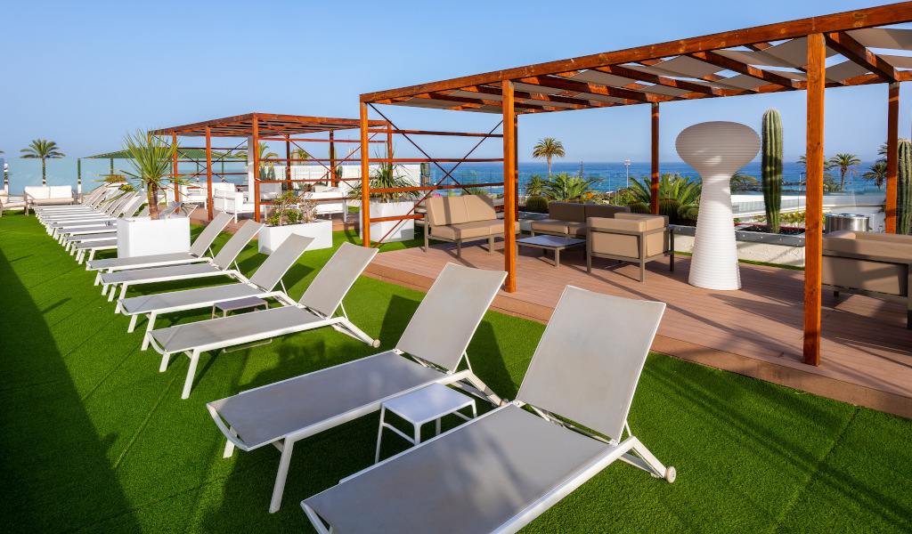 Lettini su terrazza con vista mare a Tenerife, circondati da palme e sedie.