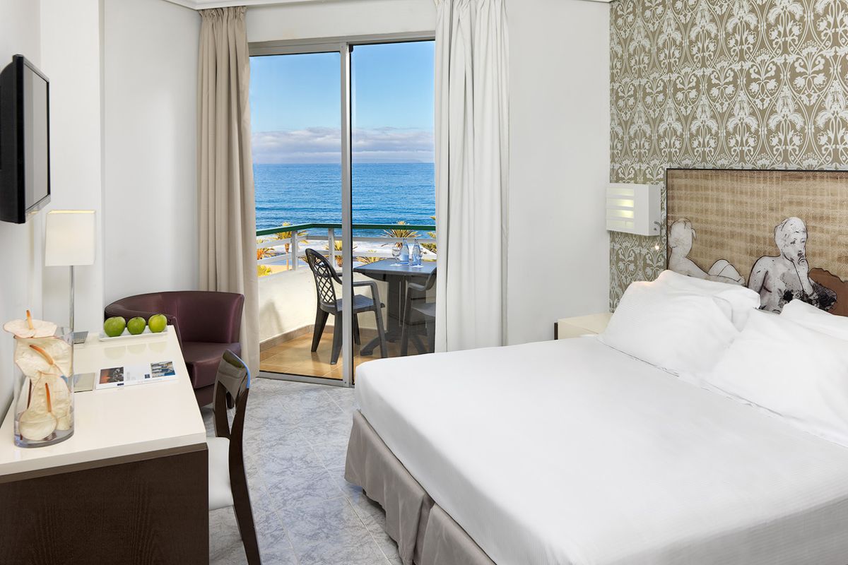 Camera d'hotel con letto, scrivania e balcone vista mare a Tenerife.
