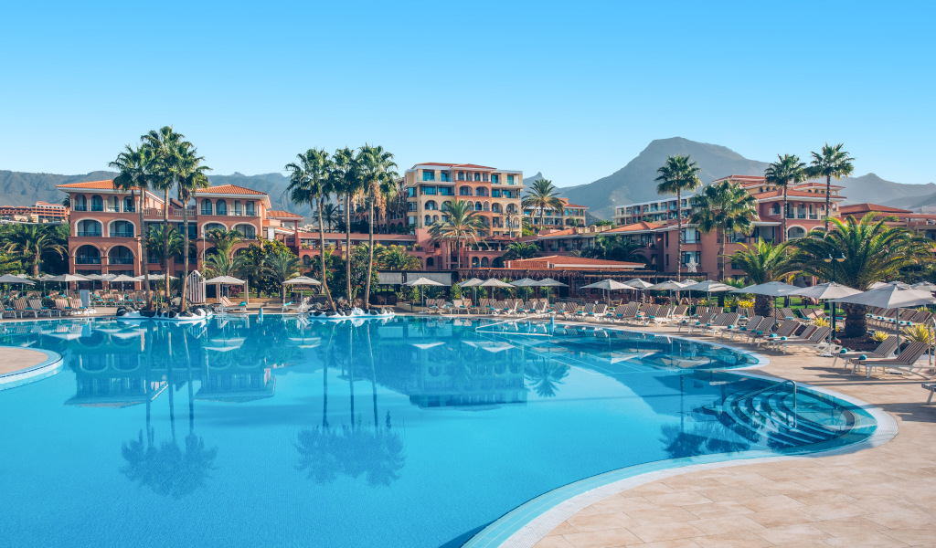 Piscina di un hotel lussuoso a Costa Adeje, Tenerife, con sedie a sdraio e palme.