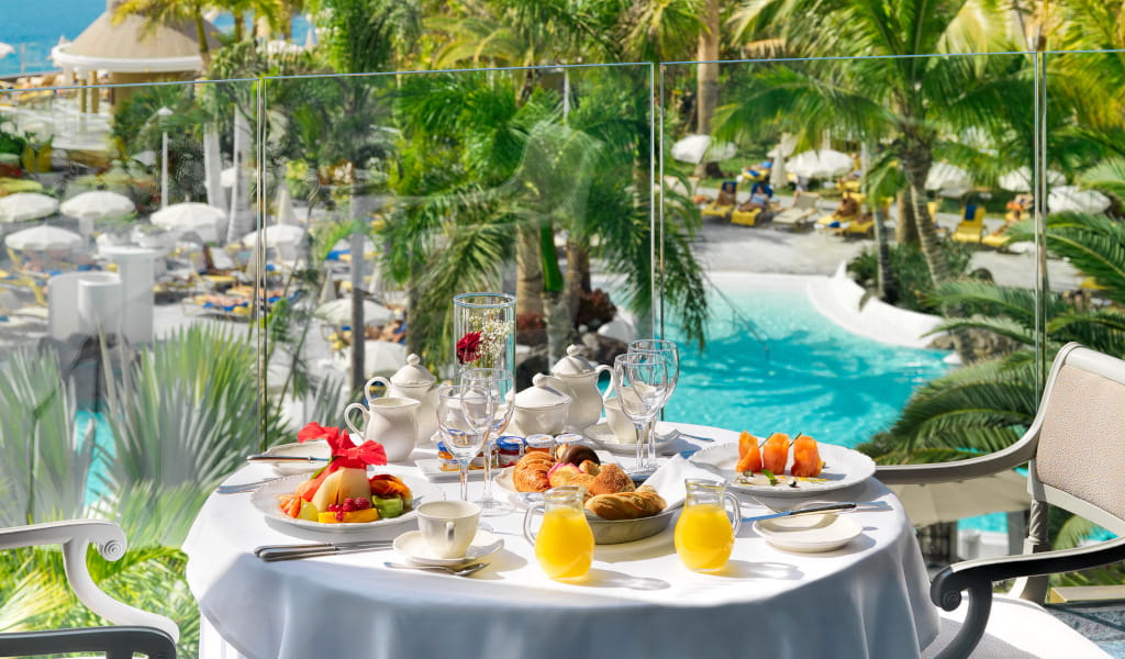 Colazione su terrazza vista piscina a Tenerife con piatti e bevande.