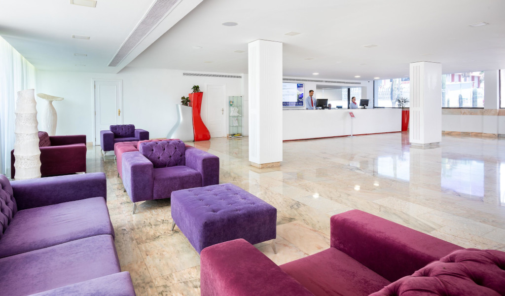Area reception spaziosa con divani viola e bancone in un hotel a Tenerife.