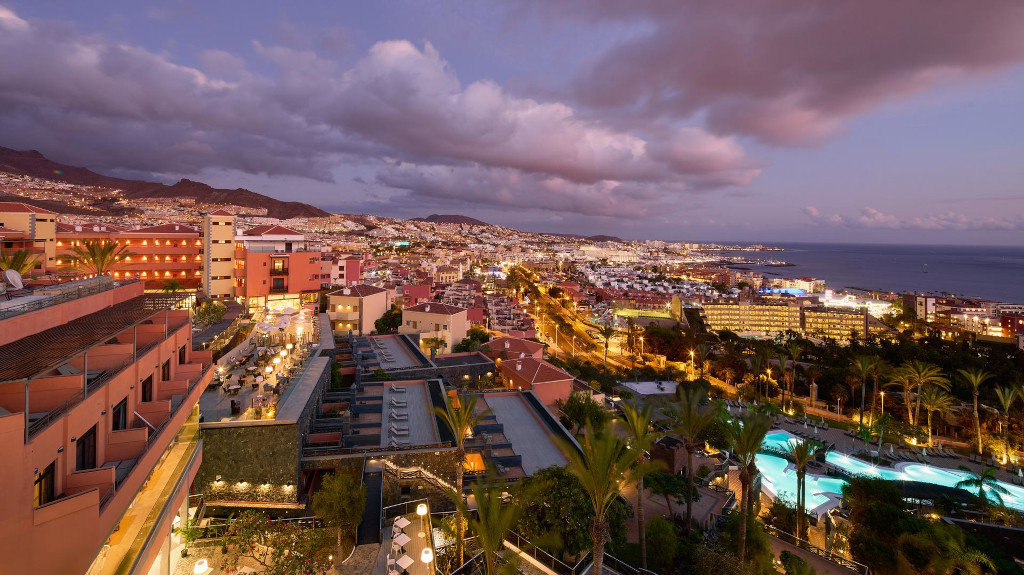 Vista serale di Costa Adeje, Tenerife, con luci della città e oceano al tramonto.