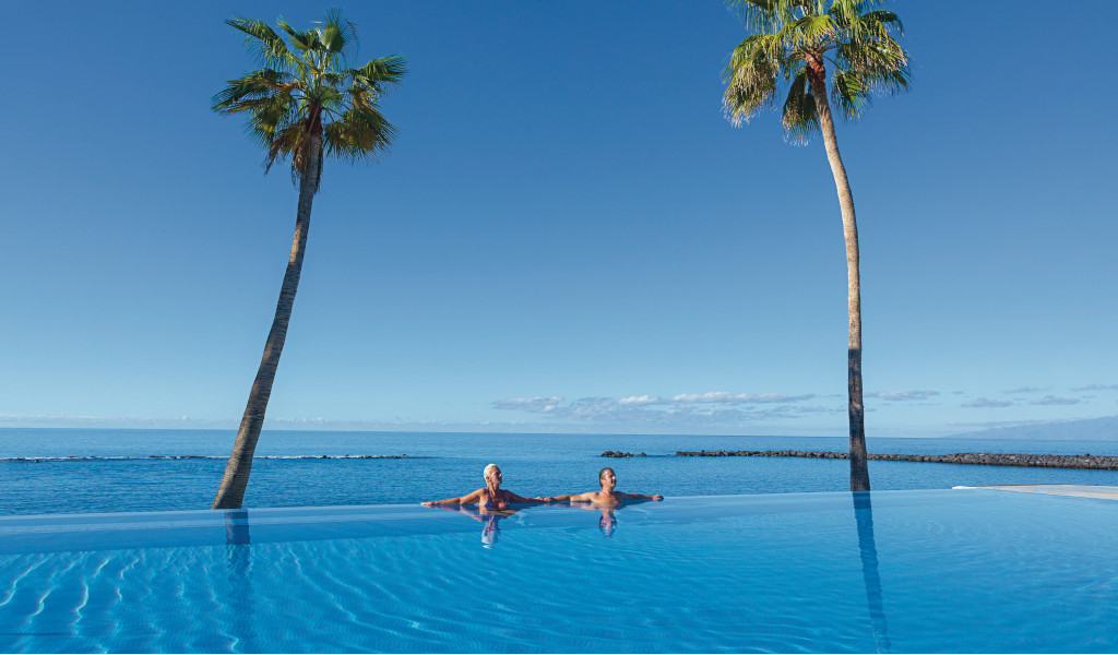 Due persone in piscina con palme e vista sul mare a Tenerife.