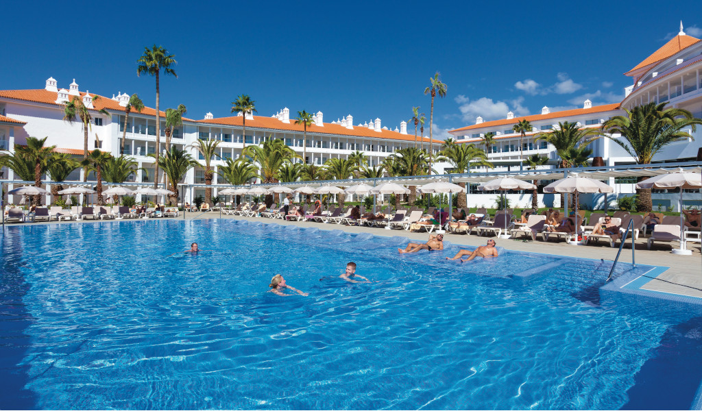 Piscina soleggiata di fronte a un hotel con palme a Tenerife.