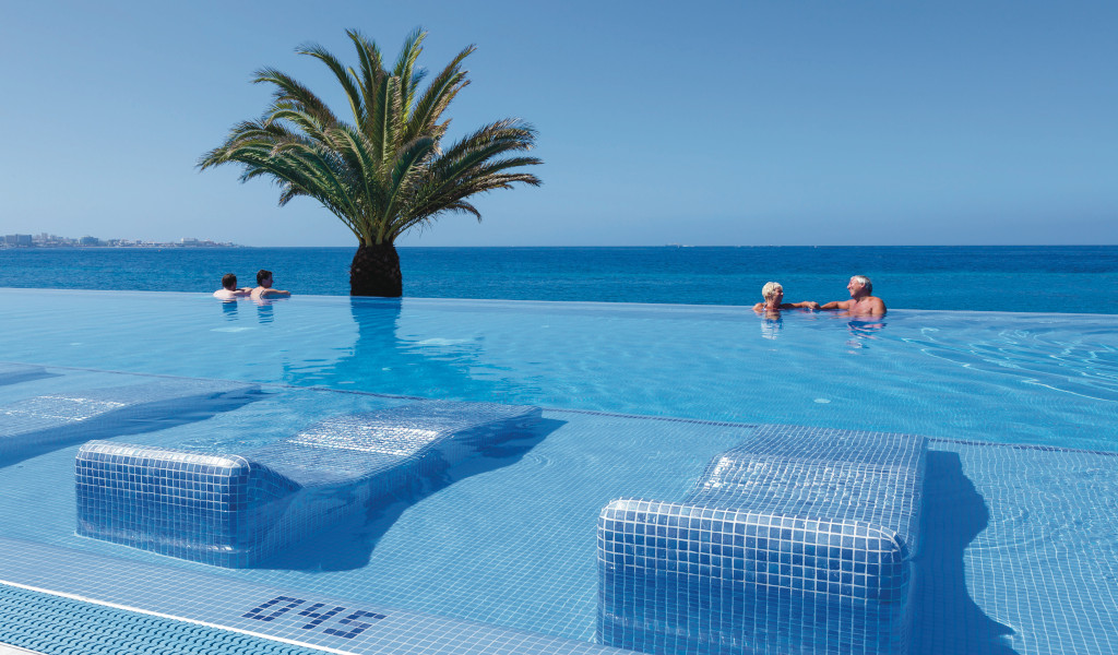 Persone in piscina a sfioro con vista mare e palma a Costa Adeje, Tenerife.