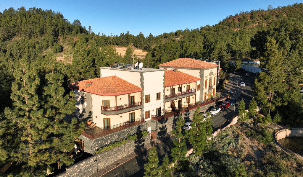 Edificio con tetto arancione a Vilaflor, circondato da alberi e colline.