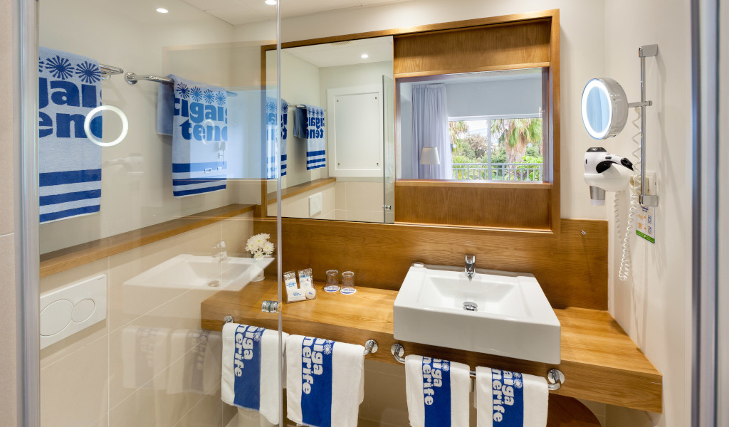 Bagno con specchio, lavandino e asciugamani blu con testo Lugano Tenerife.